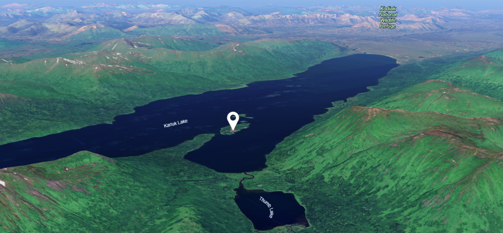 Aerial view of a lush green landscape with Katmai Lake and nearby Surprise Lake, surrounded by mountains. A map pin marks a location on Katmai Lake; Kodiak Island Wildlife Refuge is labeled in the distance.